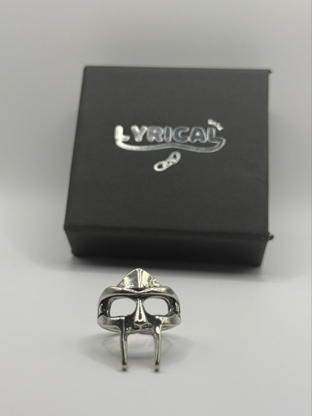 Silver ring on a white surface next to a black box with a brand logo.