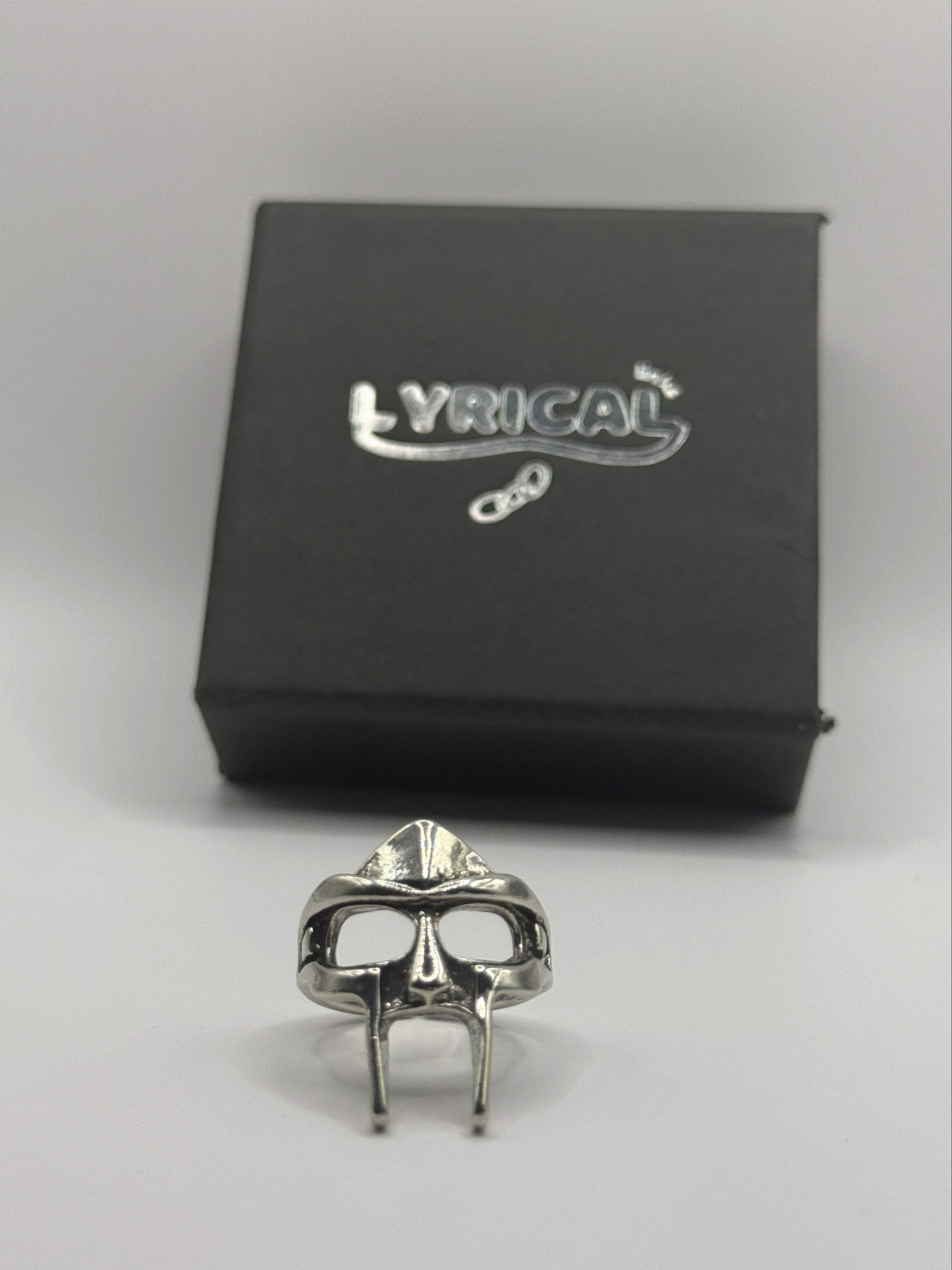 Silver ring on a white surface next to a black box with a brand logo.
